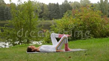 年轻女子在河岸躺在瑜伽垫上抬起腿